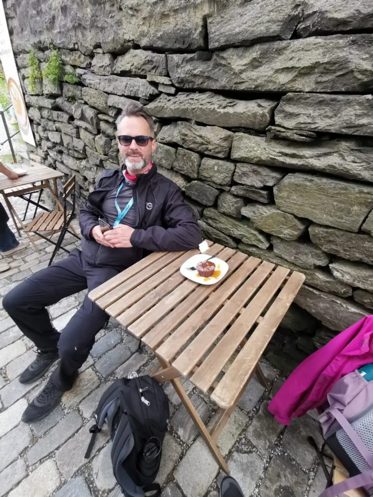 Mann sitzt an Holztisch vor Steinwand