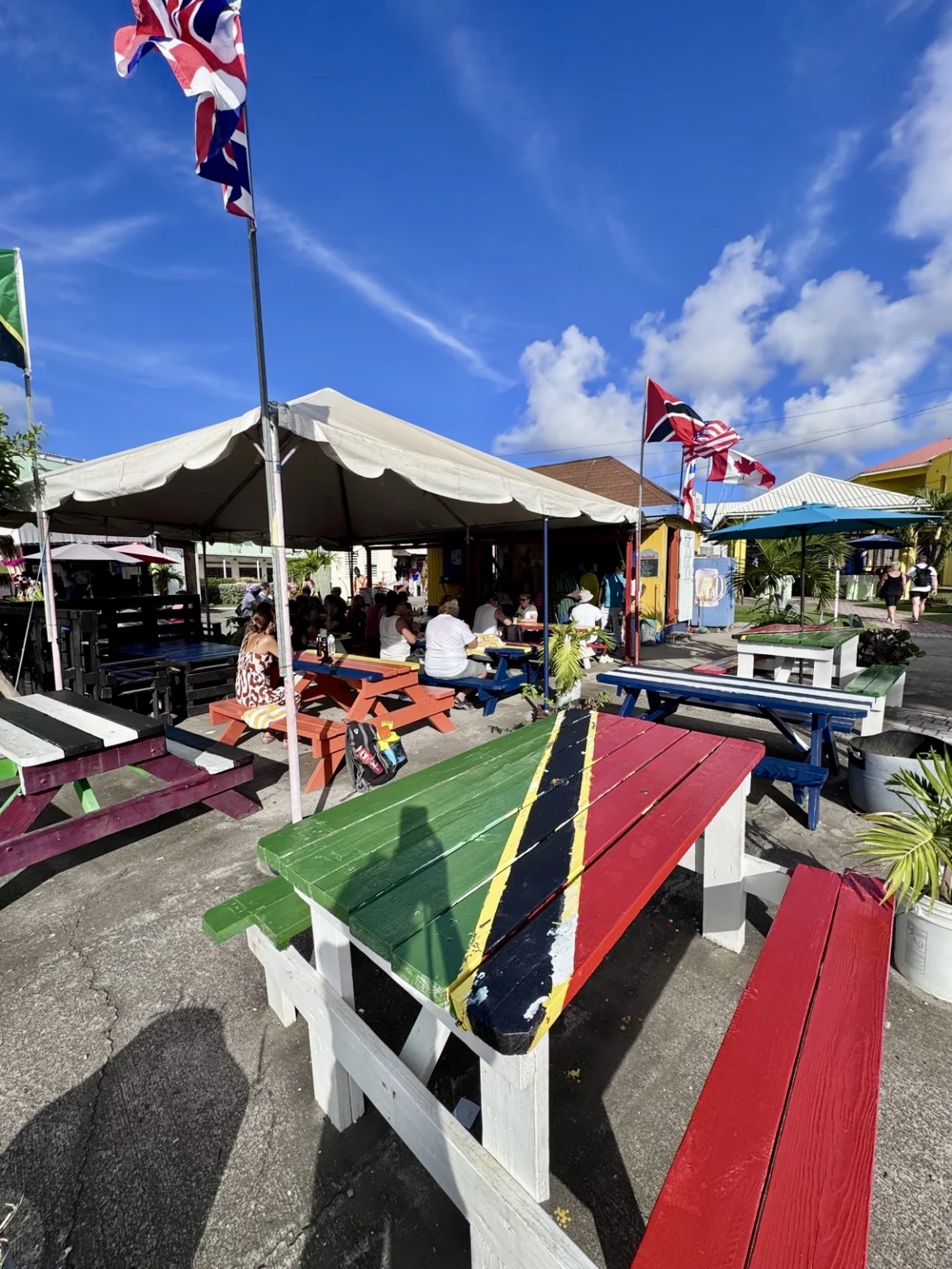 Bunter Outdoor-Markt mit rot-grünen Holzbänken und britischen Flaggen unter weißen Zelten bei blauem Himmel"