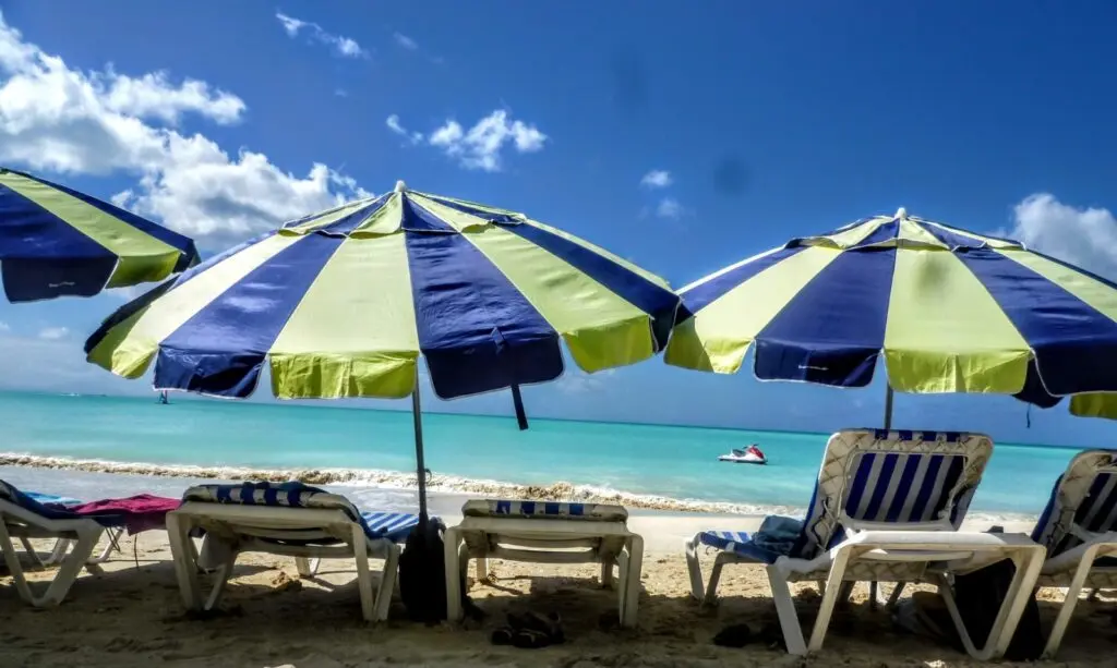Gelb-blaue Sonnenschirme und Liegen Frau am Strand mit türkisem Meer auf Antigua St. Johns
