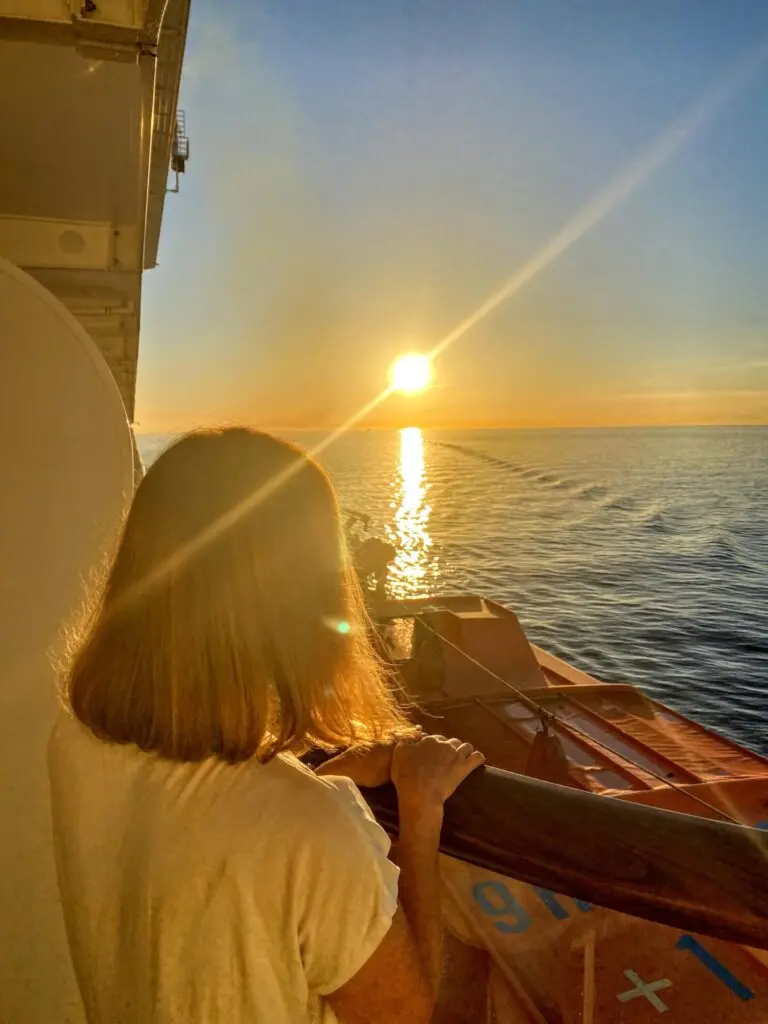 Frau schaut zum Sonnenuntergang auf Kreuzfahrtschiff