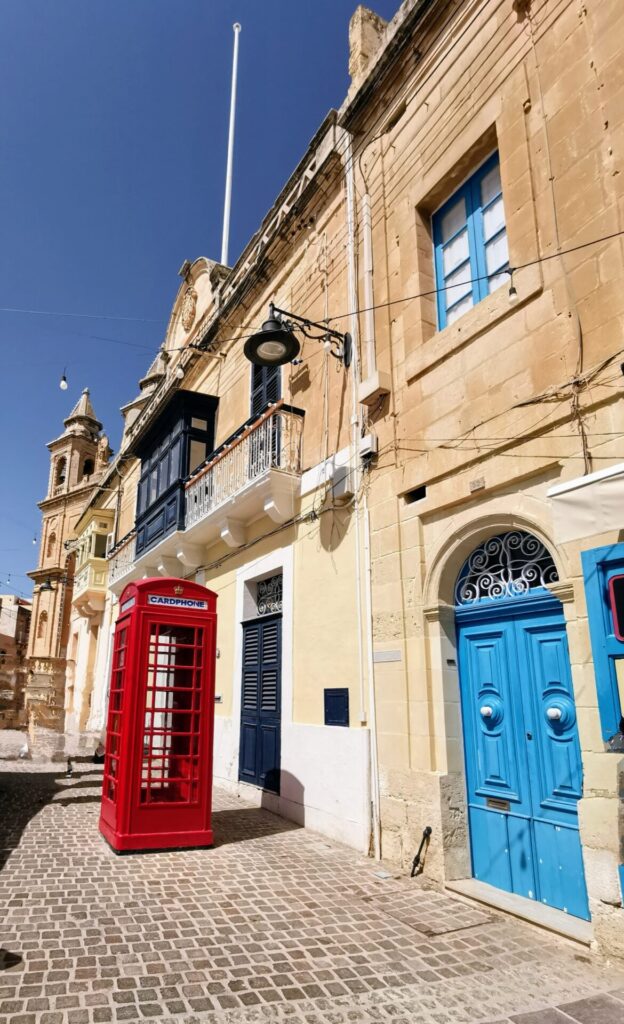 Rote Telefonzelle und Haus mit blauer Tür in der Stadt Marsaxlokk