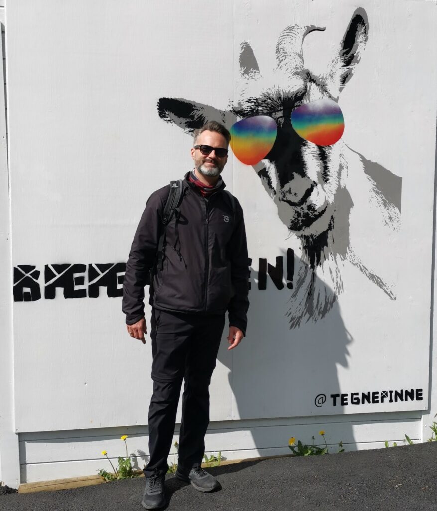 Mann vor Werbeplakat mit Ziege in Bergen